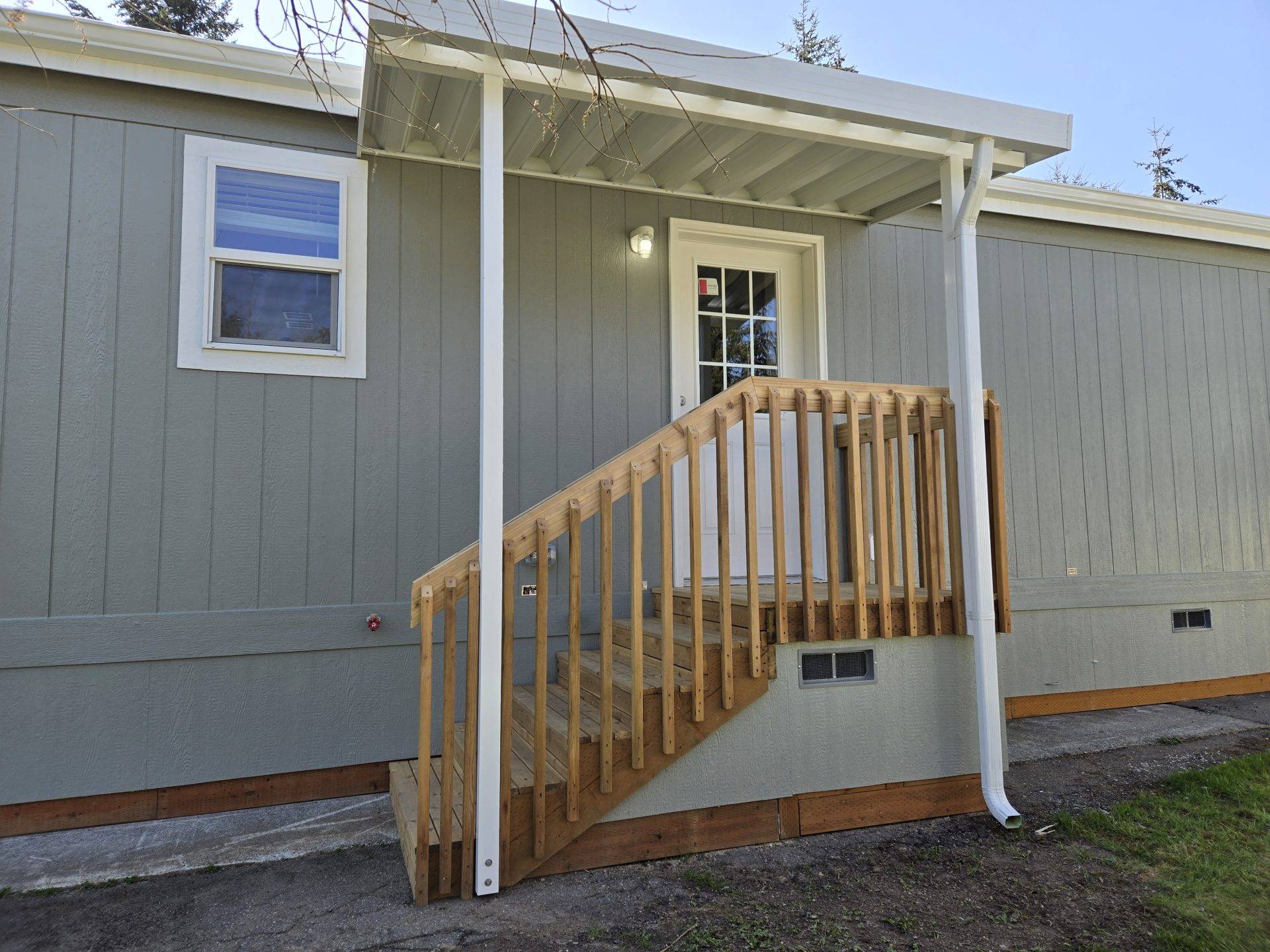 A small house featuring a porch and stairs, set against a clear sky.