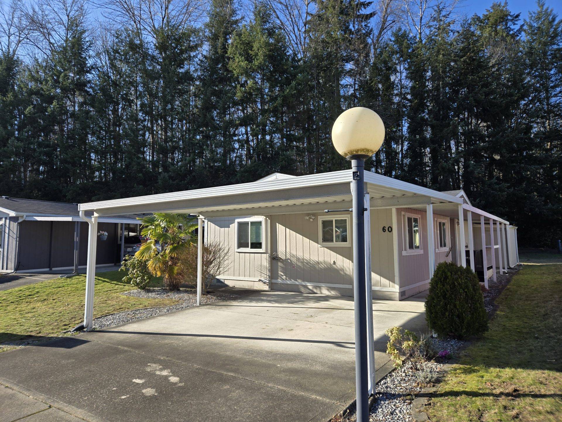 A mobile home featuring a covered porch illuminated by a light, set against a clear sky.