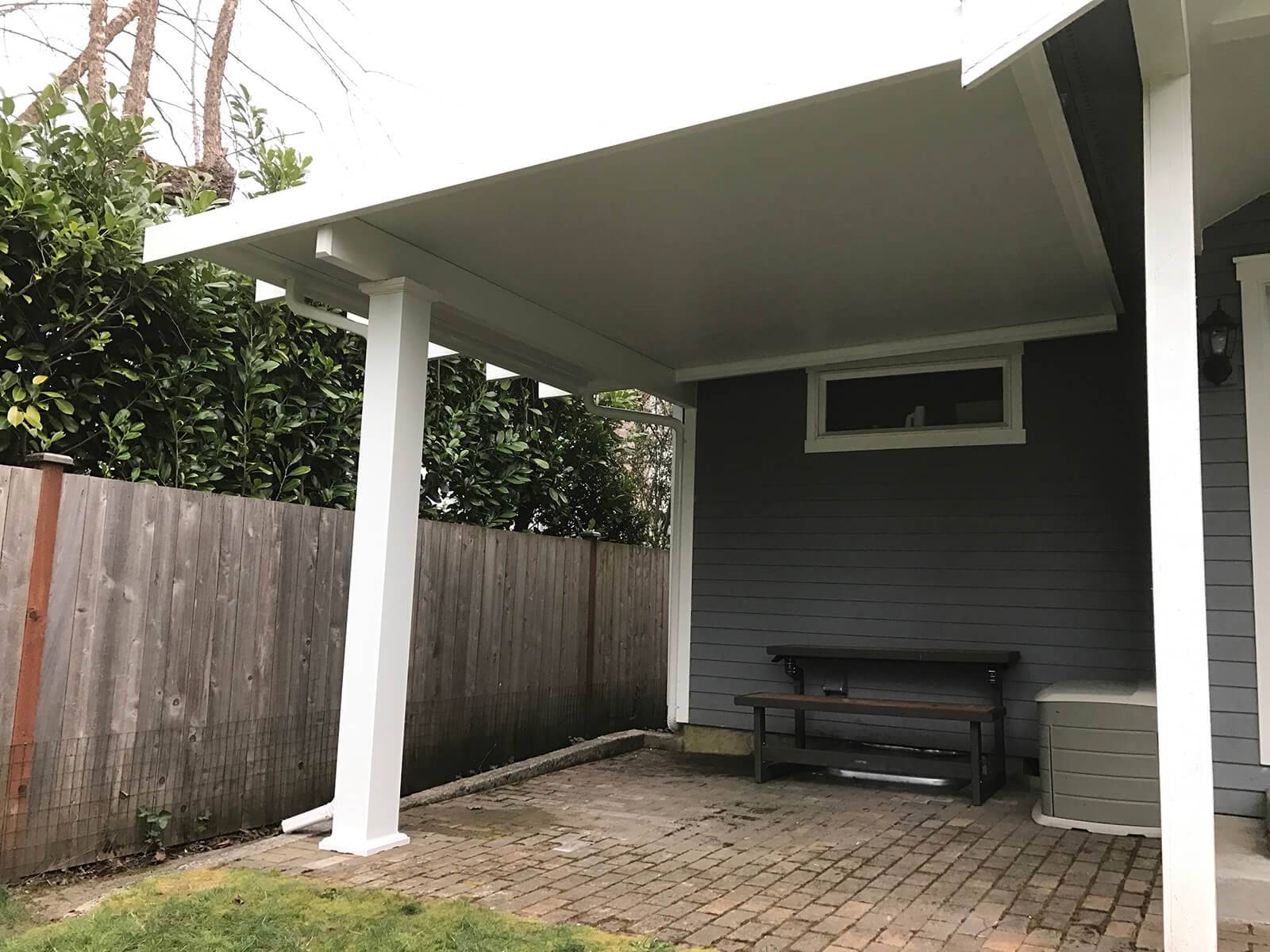 A covered patio featuring a wooden bench and a door, providing a cozy outdoor seating area.