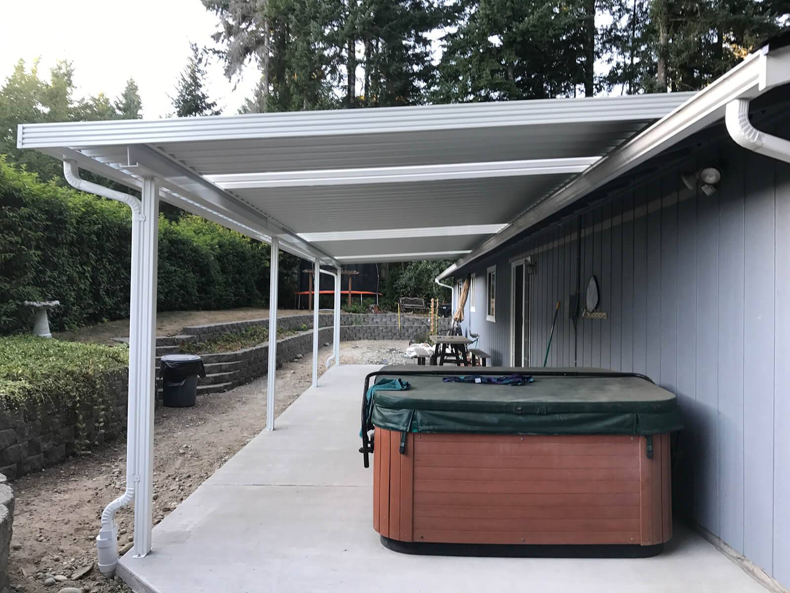 A hot tub sits beneath a covered patio, accompanied by a patio table, creating a cozy outdoor relaxation space.